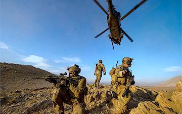 三名士兵在战场上站岗，一架直升机在上空飞行